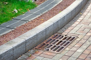 Kaldırımın kenarındaki kaldırımda, kaldırım kenarındaki kaldırım taşlarından oluşan eğimli kaldırımda rögar kapağı var. Demir ızgaralı bir fırtına kanalı..