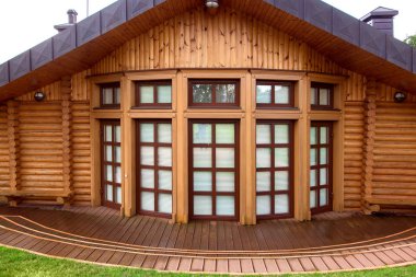 Kahverengi renkli panoramik pencereli ahşap ahşap bir ev ve camlarında beyaz panjurlar, yağmurdan sonra teras ıslaktır..