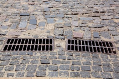 Kanalizasyon sisteminin demir ızgaraları kaldırım taşlarıyla döşenmiş, 2 kanalizasyon ızgarasının yan görüntüsü..