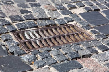 Asfalt taşlarla döşenmiş yoldaki drenaj sisteminin eski demir ızgarası, kanalizasyon ızgarasına yakın çekim..