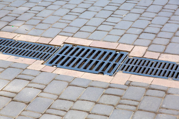 Решетка дренажной системы мощения на дорожке из квадратной каменной плитки, крупным планом дренажной системы
.