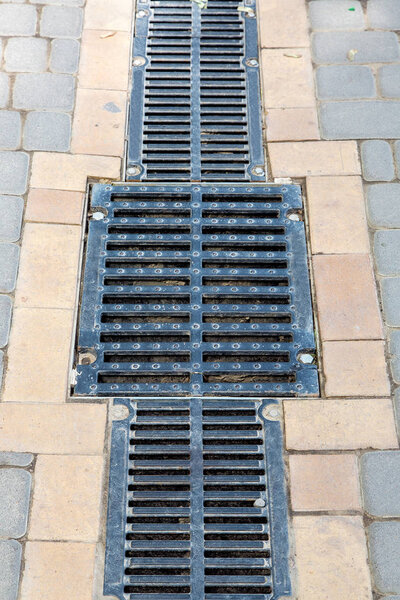 Решетка дренажной системы с решеткой люка на тротуаре из каменной плитки, крупным планом
.