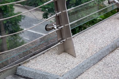 Köprünün kenarında çelik yamaçları ve granit kaldırımı olan cam bir köprünün inşaat detayları var..