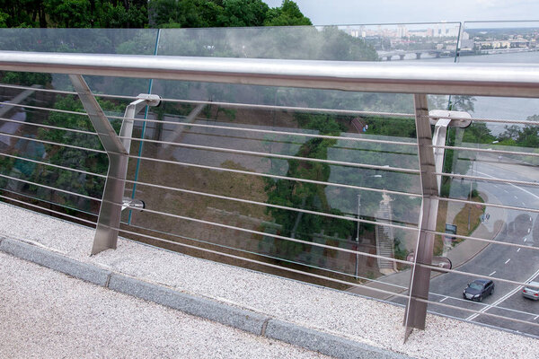 construction details of a glass bridge with steel fixtures with a railing and a granite curb at the edge of a pedestrian glass bridge, city on background nobody.