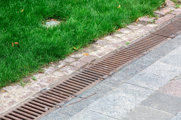 ржавчина дренажной решетки штормовой системы на пешеходном тротуаре из каменной плитки в парке рядом с зеленой травой
.