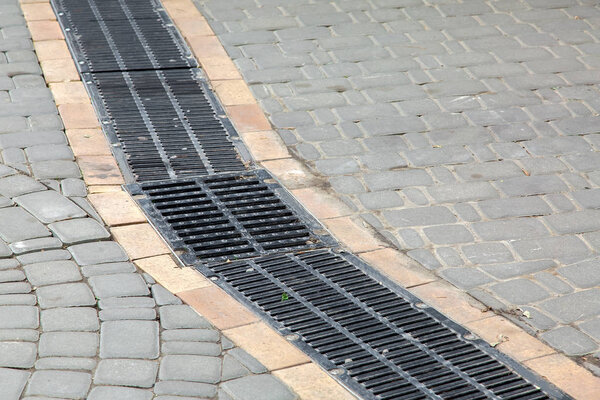 black grille drainage system installed in the pedestrian sidewalk made of stone tiles.