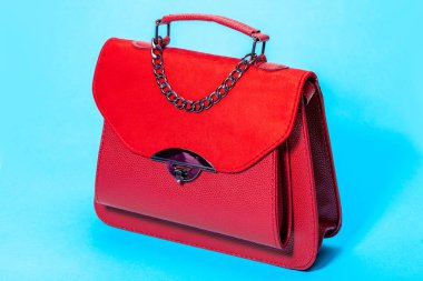 women's handbag in red leather and suede, side view 3/4 object on a blue background.