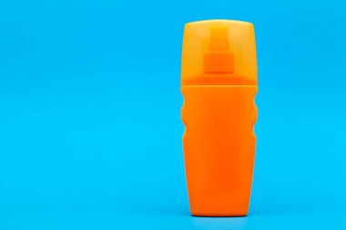 mavi arkaplanda fotokopi alanı olan turuncu, etiketsiz güneş kremi şişesi..