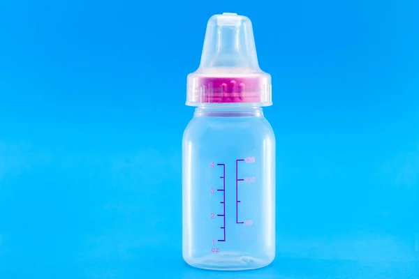feeding bottle with pacifier and measuring scale, transparent plastic bottle with a cap isolated on a blue background with copy space.