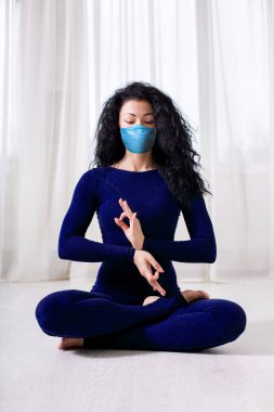 Tıbbi maskeli yalnız bir kız, covid 19 cotonavirüsünün karantinası sırasında ışık odasında yoga egzersizleri yapıyor..