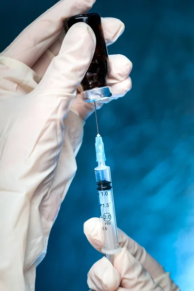 the hands in medical gloves hold a glass bottle with a vaccine and a syringe with a needle for vaccination against coronavirus, close up medical concept.