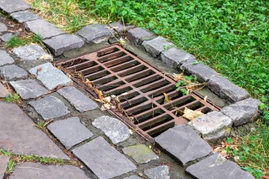 Kare kapak paslı yağmur fırtınası yapraklarla kaplı ızgara parkın kaldırımında taştan yapılmış çöplerle, kapat..