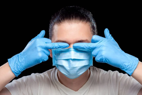 hands in gloves show obscene gesture with middle fingers covering eyes on corruption male portrait of a doctor in a medical mask, closeup isolated on black background.