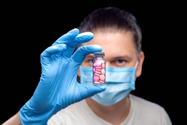 Erkek portresi. Tıbbi maskeli bir doktor. Steril eldivenle, hastalığın tedavisi için pembe haplarla dolu cam bir şişe..