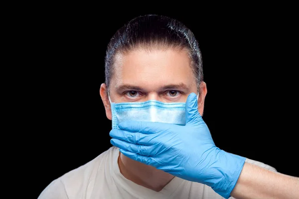 Mute male portrait doctor in medical mask and surgical glove cover his mouth with his hand isolated black background, concept silent protest italian strike due to coronavirus pandemic strain covid-19.