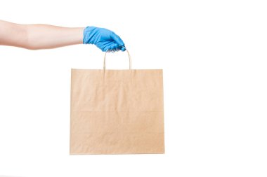 Kahverengi kağıttan bir çevre dostu paket steril eldivenli bir teslimatçının elini tutuyor. Beyaz bir arka planda kopyalanmış, virüs salgını sırasında güvenli bir şekilde teslim ediliyor..