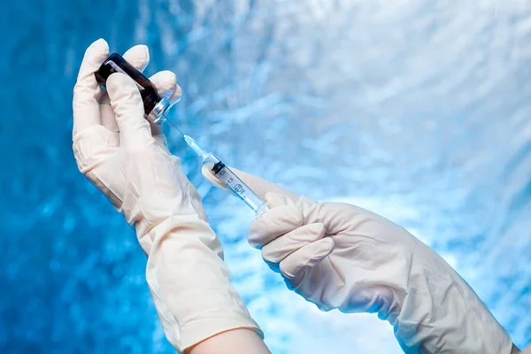 the hands in medical gloves hold a glass bottle with a vaccine and a syringe with a needle for vaccination against coronavirus strain covid-19, close up medical concept with copy space.