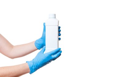 Mavi tıbbi steril eldivenli eller beyaz arka planda izole edilmiş steril dezenfektan kapaklı plastikten yapılmamış beyaz bir şişe tutuyor..