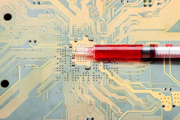 syringe with needle filled medicinal product lies on silicone printed circuit board with contact tracks of electronic equipment of modern medicine injection cyber implantation treatment of human body.