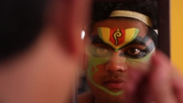 Tanečník Kathakali se dívá do zrcadla a aplikuje na obličej zelenou barvu. 