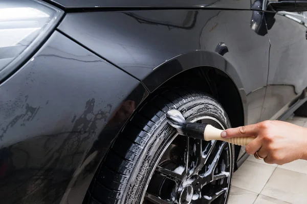 Mężczyzna pracownik myje czarny samochód ze specjalnym pędzlem do obsady — Zdjęcie stockowe