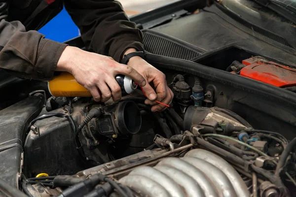 Een mannelijke monteur met een spuitbus benzine in de inname manifest — Stockfoto