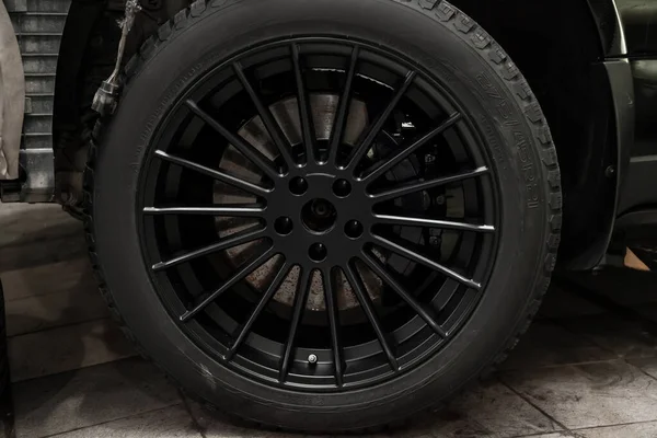 Una rueda de aleación de aluminio con neumáticos tachonados de invierno en un coche negro —  Fotos de Stock