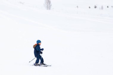 Küçük bir çocuk kayakçı dağdan aşağıya kayıyor. 