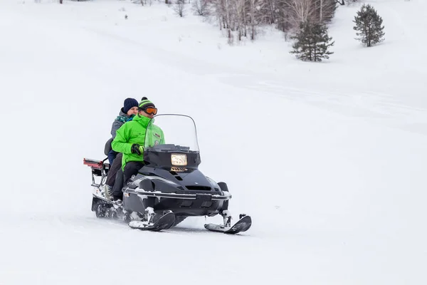 Οι άνθρωποι σε ένα snowmobile ανεβαίνει ανηφόρα πάνω από το λευκό χιόνι σε ένα σπορ — Φωτογραφία Αρχείου