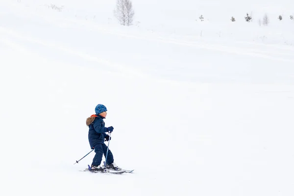 Egy kisgyerek síelő csúszik le a hegyről a fehér hó felett. — Stock Fotó