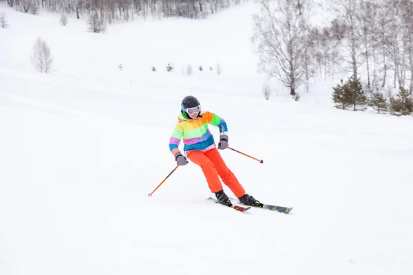 A woman skier slides down the mountain over white snow in a spor — стокове фото