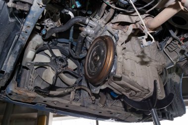 A car raised on a lift for repair and under it a detached Transm