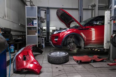 Red used car with an open hood raised on a lift for repairing th