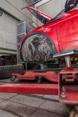 Red used car with an open hood raised on a lift for repairing th