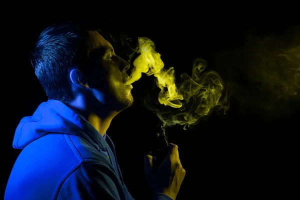Ο άνθρωπος καπνίζει ένα ηλεκτρονικό τσιγάρο στο σκοτεινό φόντο. Γιο — Φωτογραφία Αρχείου