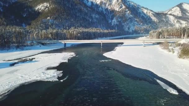 Volo sul fiume Katun coperto di ghiaccio e neve con un ponte automobilistico sul quale il trasporto viaggia sulle montagne dell'Altai . — Video Stock