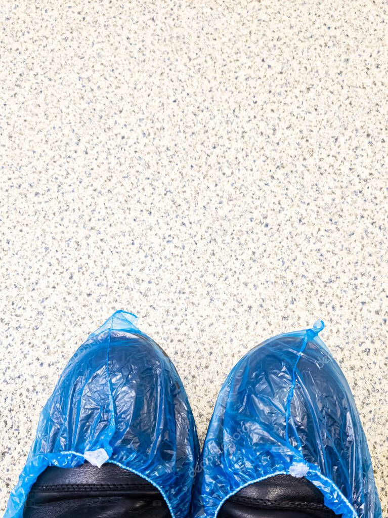 Top view of two legs in boots wrapped in blue shoe covers in a hospital while waiting for a doctor's appointment.