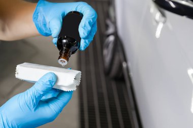 Boyayı korumak için kimyasal bileşimi olan bir erkek işçi tarafından süngerin üzerine bir damla nano seramik boya damlatılıyor. Şişenin boynundan sarkıyor..