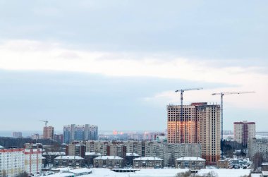 Şehir manzaralı güzel bir akşam manzarası. Vinçli yüksek bir bina inşa ediliyor ve pencereler kışın gün batımını yansıtıyor..