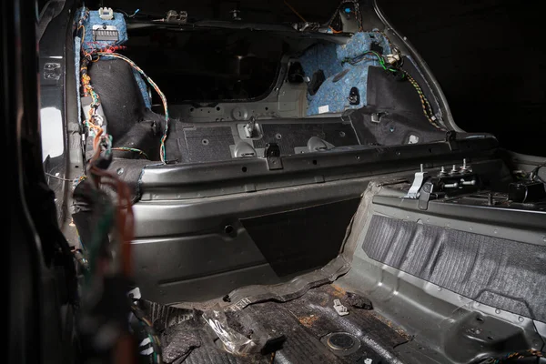 The rear body interior part of the cabin inside the sedan car, dismantled trim with colored wires, prepared for the replacement and installation of noise insulation in auto service for tuning vehicles