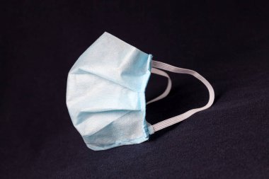 Koronavirüs gribi salgınının yayılması sırasında bakteri ve virüse karşı kişisel koruma sağlamak için tıbbi tek kullanımlık profesyonel maske. Siyah arkaplanda mavi renkte solunum cihazı.
