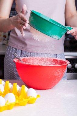 Evde, mutfakta paskalya pastası pişirmek. Yeşil bir süzgeçten geçen unu, kadınların elinde kırmızı bir klozete yerleştirmek. İçindekilerin yanında, sarı bir alt tabakadaki yumurtalar..