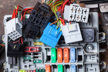 Çok renkli elektrik kabloları - sarı yeşil ve kırmızı, gri mavi ve siyah konnektörler ve atölyede araba tamiri ve elektrik devresi kontrolü için tutucuları olan panelde sigorta kutuları var.
