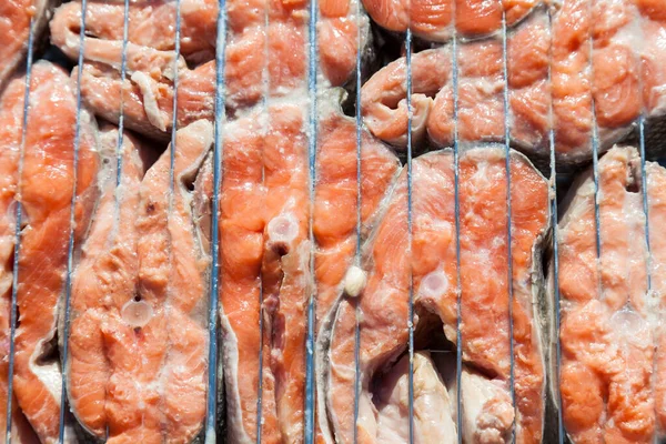 Close-up of fresh coho salmon steaks as a background on a barbecue metal grill - appetizing pieces of fish on an open red fire baked during cooking.