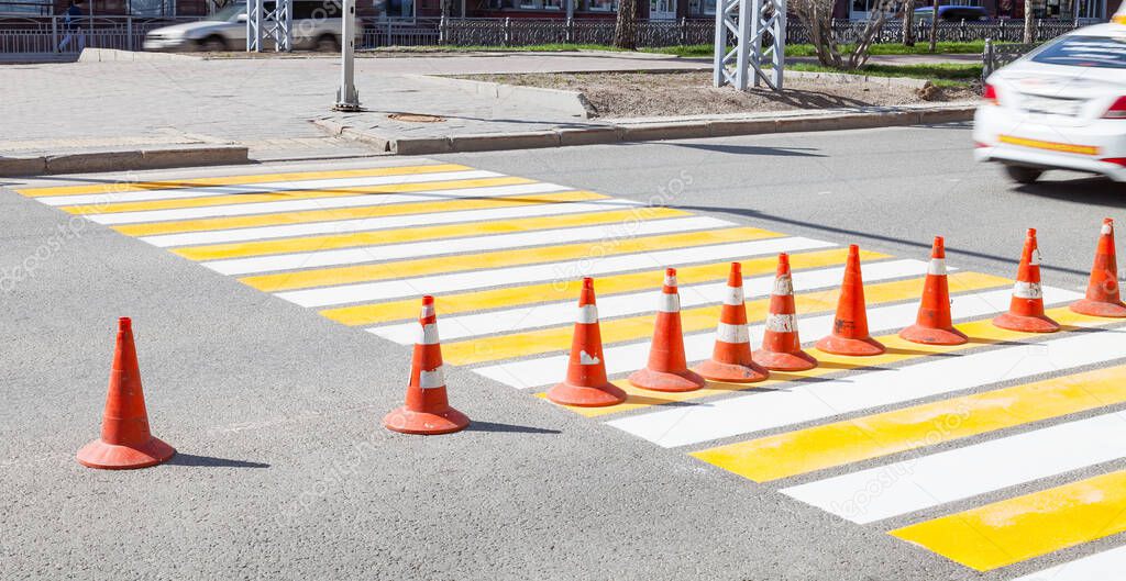 The white-yellow paint applied to the pedestrian crossing, a series of cones protects the dry marking area from the freshly painted one. Reconstruction of the roadway.