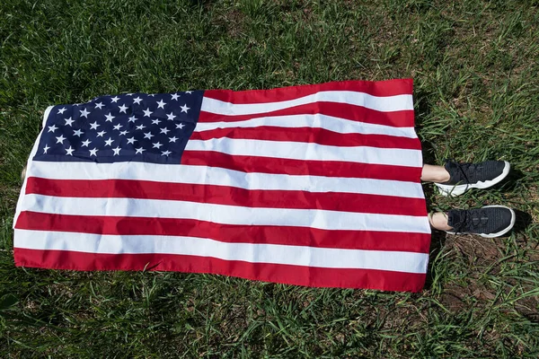 緑の芝生の上の女の子の体はスニーカーに足を突き出しているアメリカの旗で覆われたクエストの面白いアクション 舞台犯罪現場 — ストック写真