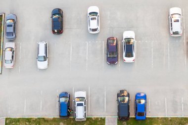 Yarı boş bir asfalt otoparkın en üst görüntüsü. Bir yaz günü, konut binasının yakınına park edilmiş siyah beyaz ve mavi arabalar..