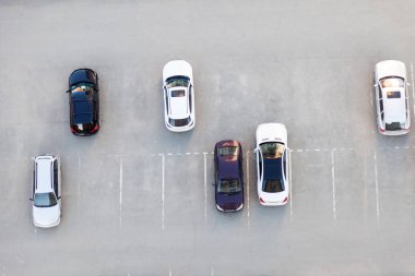 Boş alanları olan asfalt bir otoparkın üst görüntüsü ve konut binası veya süpermarket yakınlarındaki siyah beyaz ayakta duran arabalar..