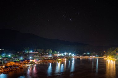 Gece manzarası ve yıldız takımyıldızları. Dağların ortasında küçük bir köy. Büyük bir nehir ve Ban Rak Thai şehri, Mae Hong Son, Tayland.