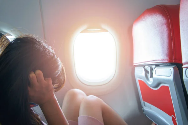 Portrait of a woman sitting on a plane by the window is stressed worry uneasy dismal unhappy upset expression sunlight and flare background concept Travel.